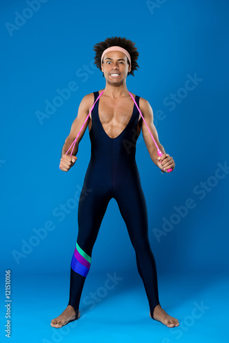 Sportive african man posing with skipping rope over blue background.