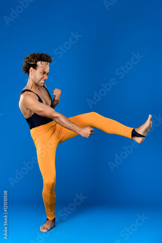 Sportive african man training martial poses over blue background.