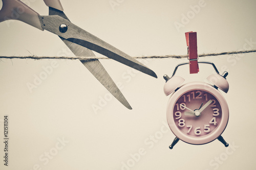 Fotografie hand cutting a rope with a clock hung on by a wooden clip - importance of time