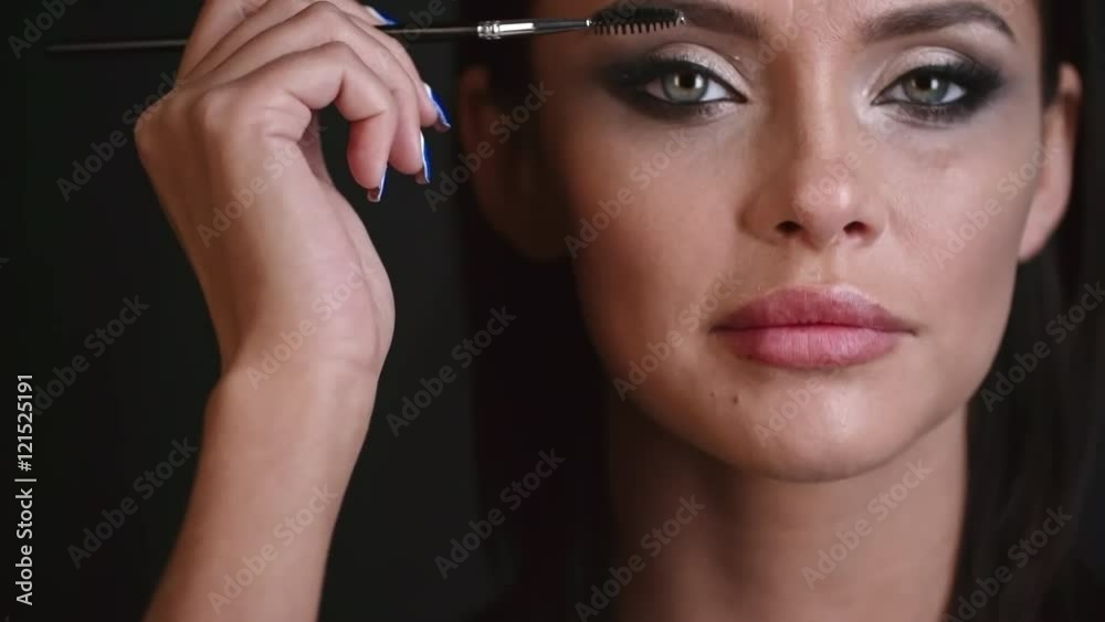 Closeup of woman with professional makeup brushing her eyelashes and then looking at the camera and smiling Closeup of woman with professional makeup brushing her eyelashes and then looking at the camera and smiling
