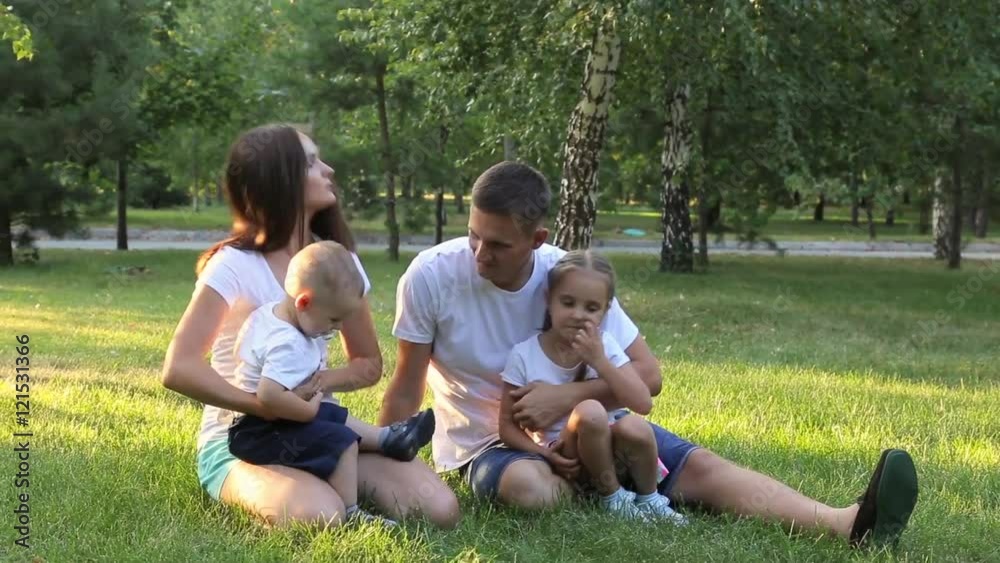 Young happy family of four sitting on the lawn in the park. Young happy family of four sitting on the lawn in the park.
