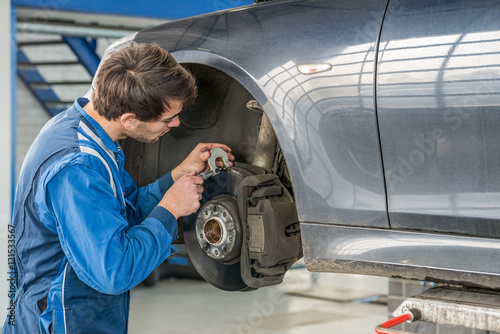 Car Mechanic Examining Brake Disc With Caliper