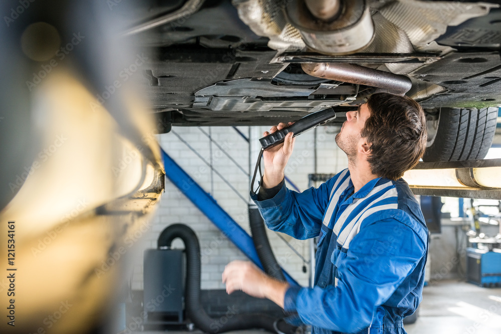 Mechanic With Flashlight Examining Under The Car Mechanic With Flashlight Examining Under The Car