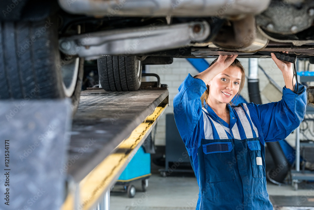 Female Mechanic Working Under Car On Hydraulic Lift Female Mechanic Working Under Car On Hydraulic Lift