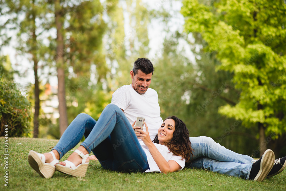 Young couple texting in the smartphone and relaxing together outdoor. Man and woman enjoying summer or spring leisure and tranquility. Young couple texting in the smartphone and relaxing together outdoor. Man and woman enjoying summer or spring leisure and tranquility.