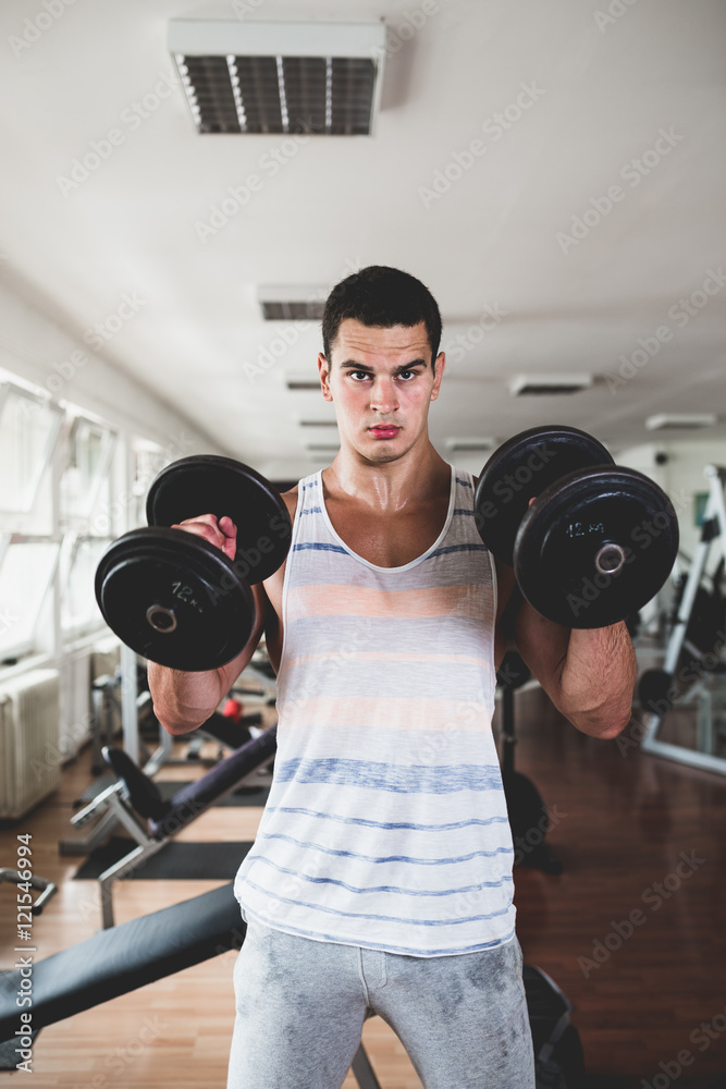 Young attractive adult man exercising and doing weight lifting at fitness gym. Sport training indoors. Young attractive adult man exercising and doing weight lifting at fitness gym. Sport training indoors.