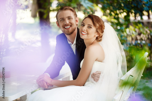 Young beautiful newlyweds smiling  embracing  sitting in cafe outdoors.