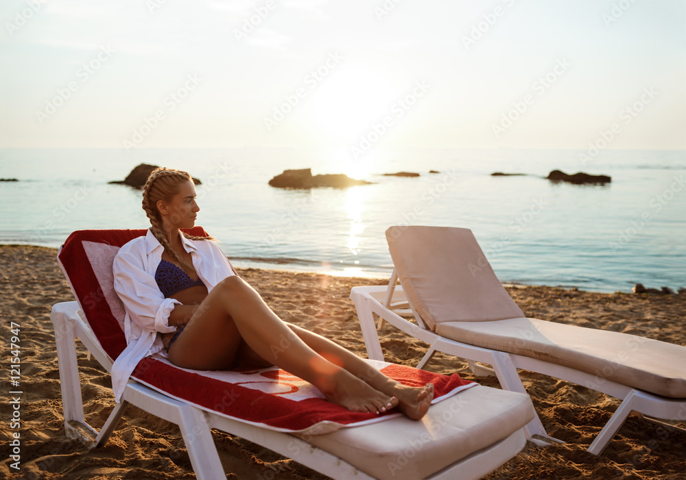 Beautiful blonde girl in swimwear lying on chaise near sea.