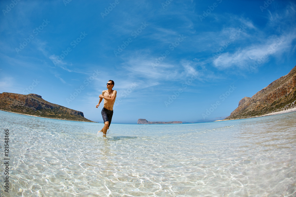 strong athletic man with bared torso running on the beach along the sea front