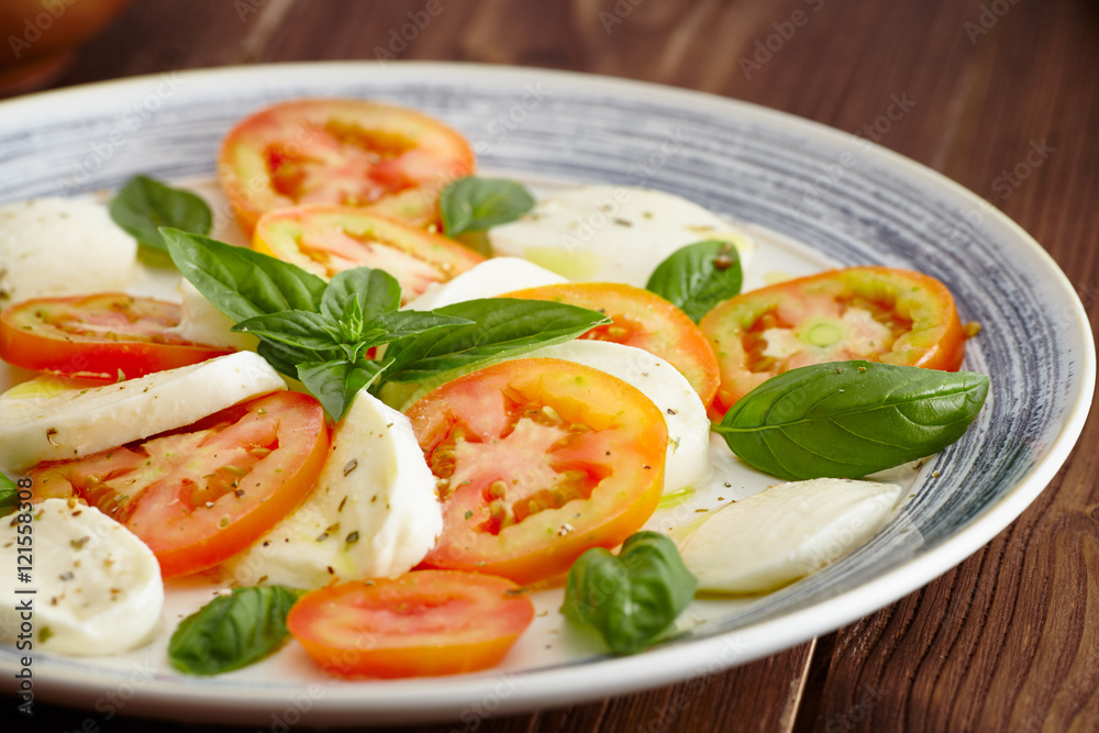 Caprese salad in a blue pastel plate on an old wooden table, with salt and pepper Caprese salad in a blue pastel plate on an old wooden table, with salt and pepper