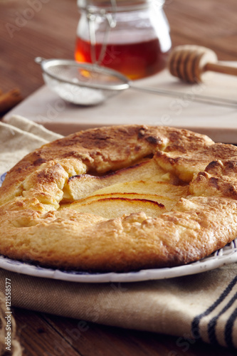 handmade apple pie on a dish over a napkin in a country style, cinnamon and hony in the background