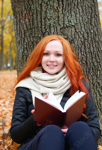 girl with book sit on yellow leaves in autumn forest