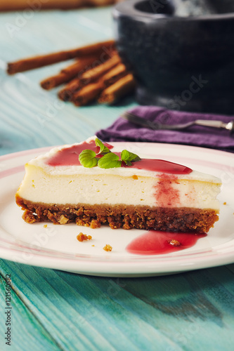 new york cheesecake with cherry sauce on a plate on a blue wooden table, full cake in background photo