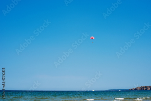 Parachuting over a sea, towing by a boat. Paragliding in the clear sky above the sea. Riding on a parachute behind a boat.