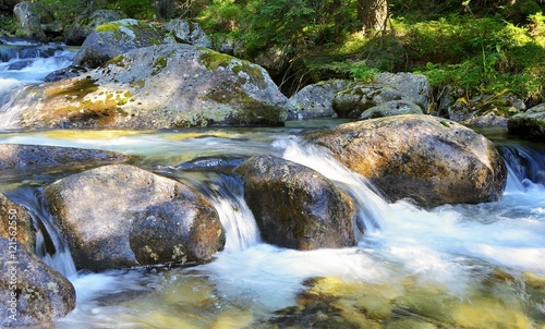 Long exposure shot of flowing water over rocks in the stream. Long exposure make the blurry effect of flowing water. Mountain stream flowing down from hill to valley.