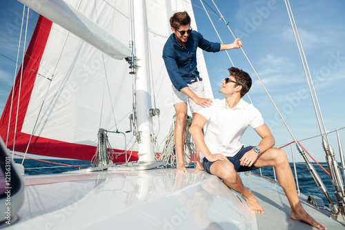 Two young handsome happy men standing on the yacht