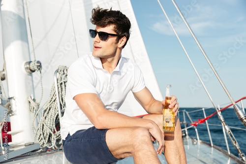 Handsome young man drinking beer while resting on the yacht