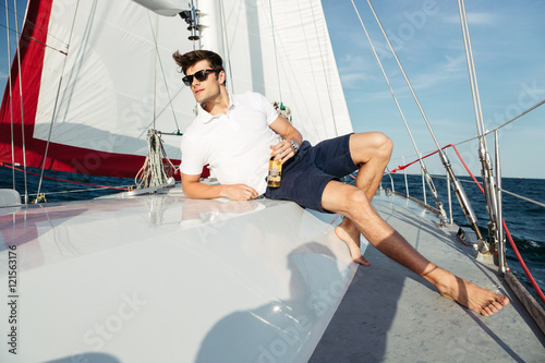 Handsome young man drinking beer while resting on the yacht