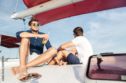 Two men friends drinking beer while resting on the yacht