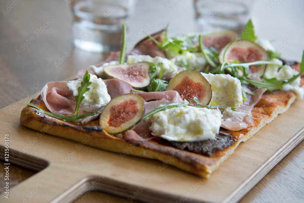 Buffalo mozzarella pizza with prosciutto and fig. Daylight. Wooden plate and table.