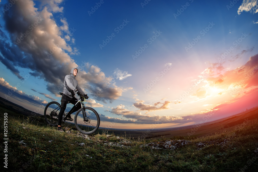 Obraz premium cyclist standing with mountain bike on trail at sunset