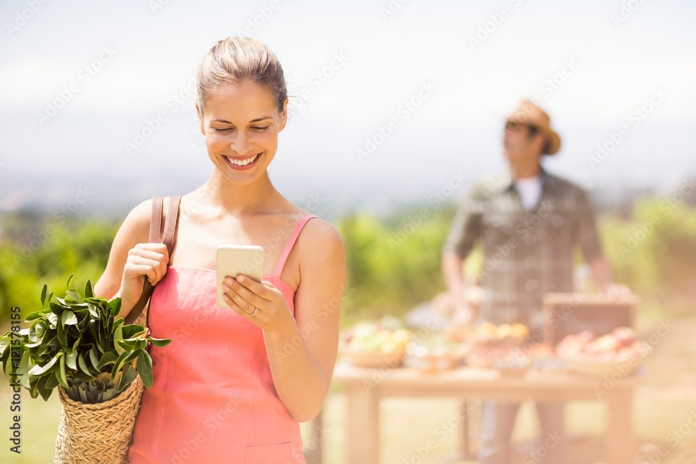 Fototapeta premium Female customer using mobile phone in front of vegetable stall