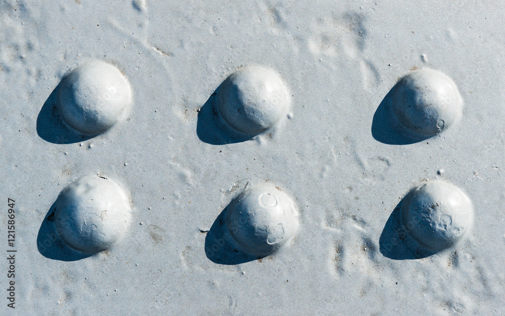 Sunlit gray painted surface with six rivet heads