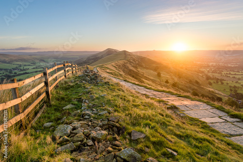 Stone footpath and wooden fence leading a long The Great Ridge in the English Peak District.