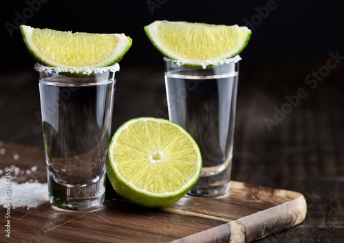 Tequila silver shots with lime slices and salt on wooden board photo