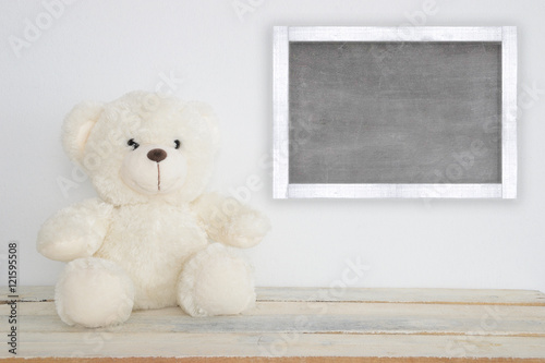 A teddy bear on a wooden table and a blackboard with empty copy space for Author's text.