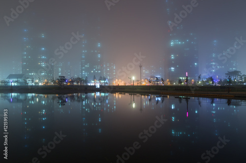 Foggy view of a park, skyscrapers and reflections on a lake in Incheon, South Korea in the evening.