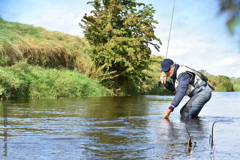 Fly-fisherman catching trout in irish river Fly-fisherman catching trout in irish river