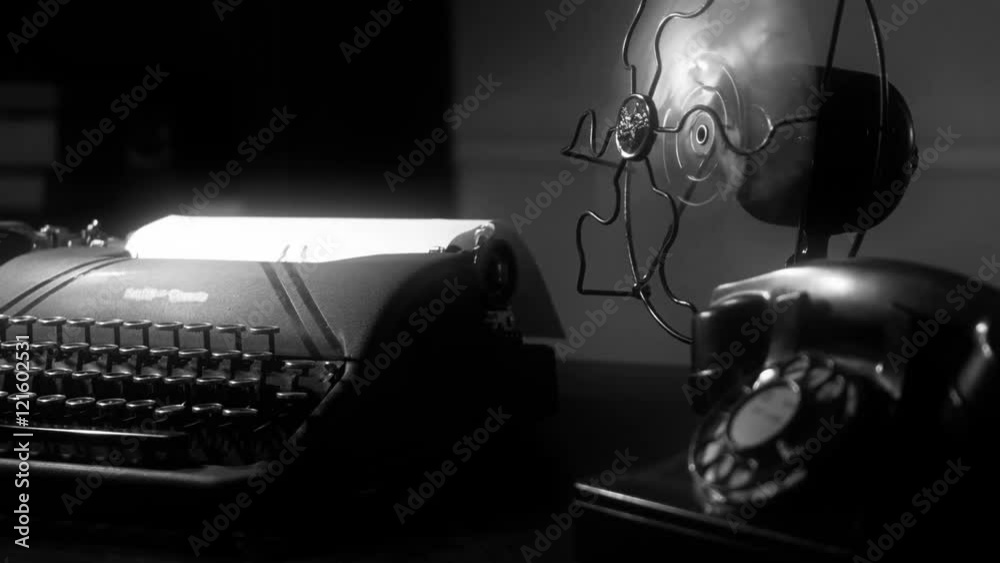 Radial dolly move of a desk with an old manual typewriter and vintage electric fan in dimly lit room. film Noir at 4k