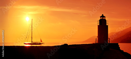 silhouettes of sailing and lighthouse at sunset