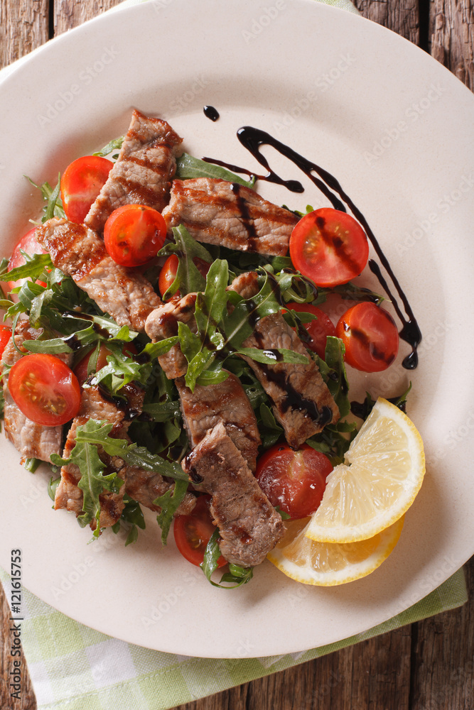 Warm salad of grilled beef with arugula and tomatoes close-up. Vertical top view
