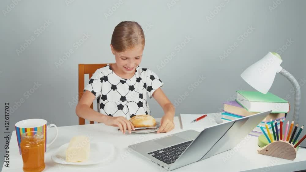 Schoolgirl making sandwich with butter sitting at the desk in and smiling in the evening Schoolgirl making sandwich with butter sitting at the desk in and smiling in the evening
