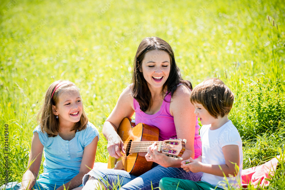 Mother playing guitar in nature to children Mother playing guitar in nature to children