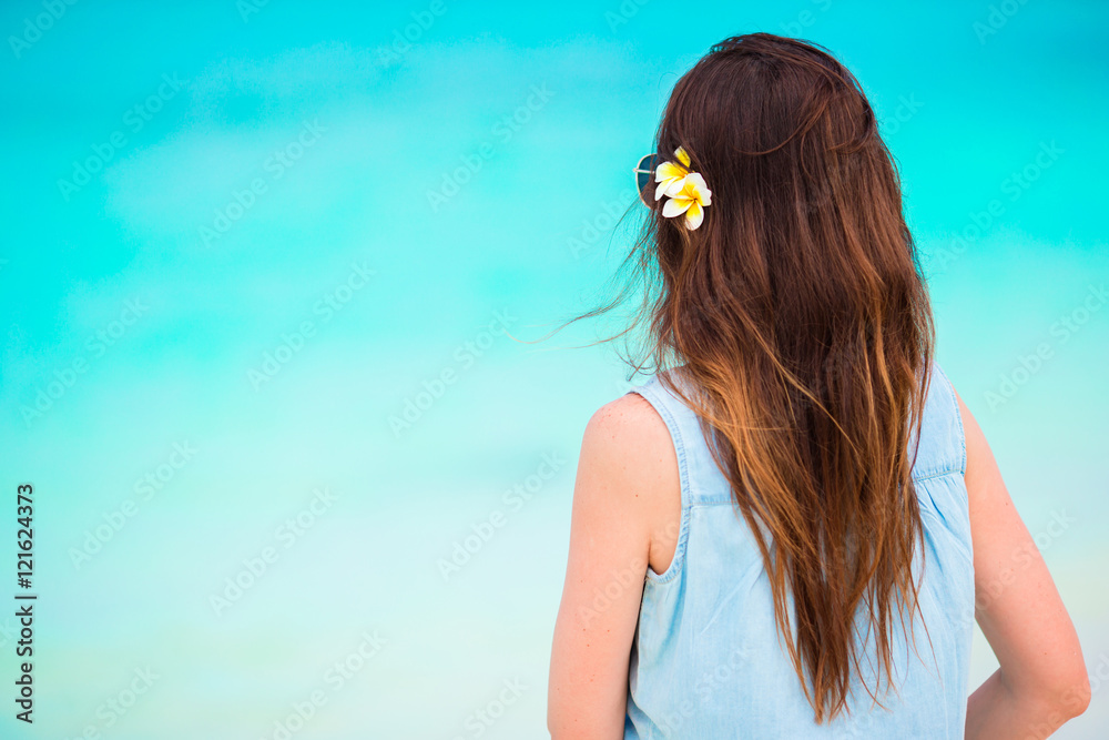 Naklejka premium Young beautiful woman during tropical beach vacation. Enjoy suumer vacation alone on the beach with frangipani flowers in her hair
