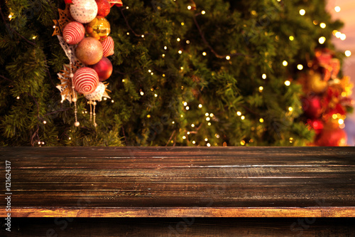 Christmas and New year background with empty dark wooden deck table over christmas tree and blurred light bokeh. Empty display for product montage. Rustic vintage Xmas background.