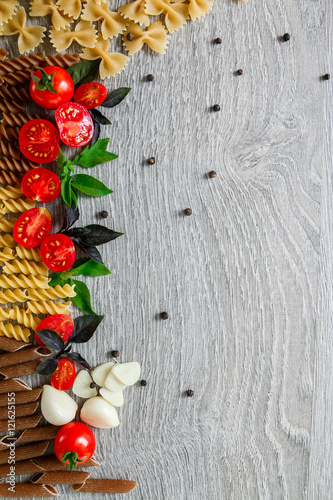 Mixed of two colored pasta near tomatoes, garlic and basil on grey wooden  background. Raw  frame. Copy space.