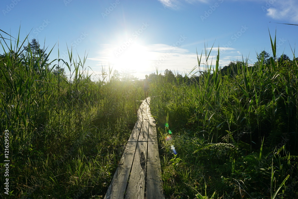 Backlit sunrise image of man running on mountain boardwalk trail 