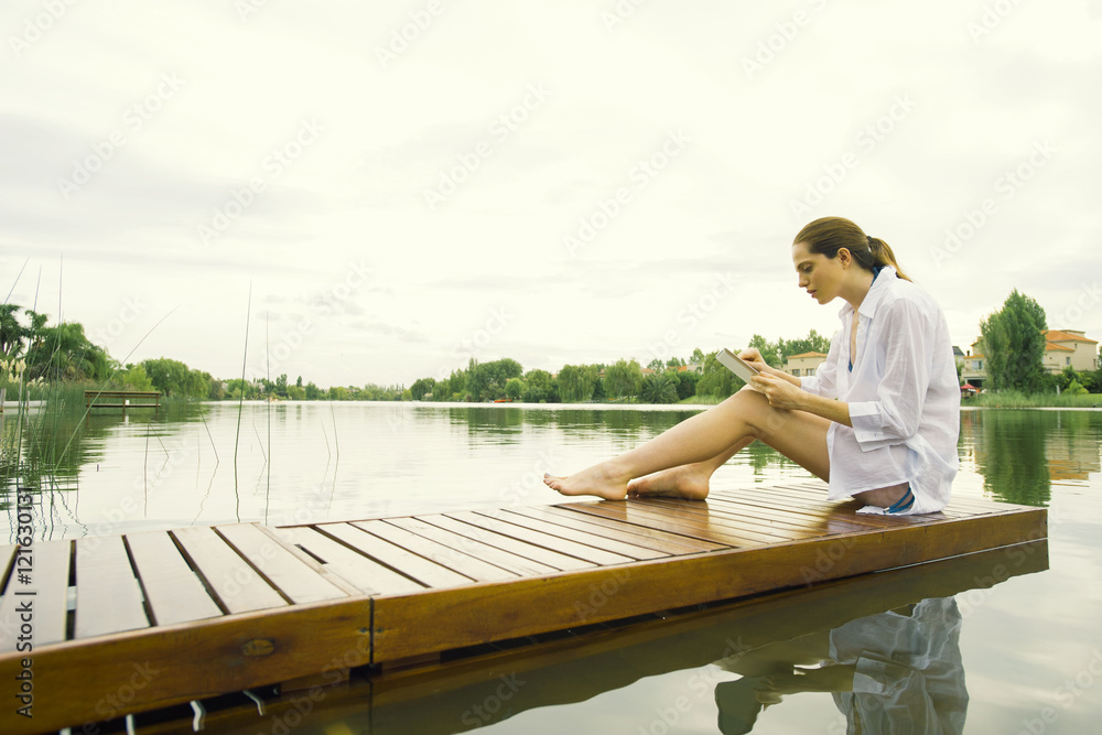 Woman sitting on lake dock using digital tablet Woman sitting on lake dock using digital tablet