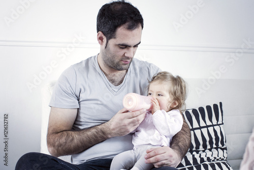 Father holding baby girl on lap, feeding her with bottle photo