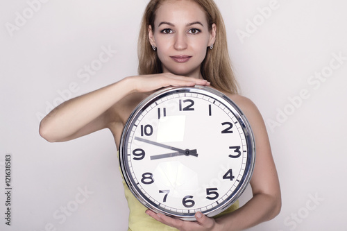 Beautiful young woman looking at a large silver retro clock that she is holding, she wonders how much time passed