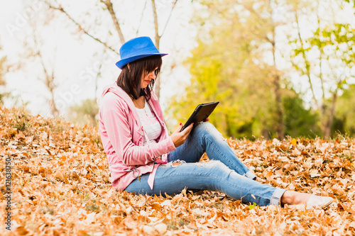 beautiful young woman with a tablet sitting in the autumn park.