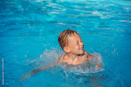 Happy kid playing in blue water of swimming pool. © nata_zhekova