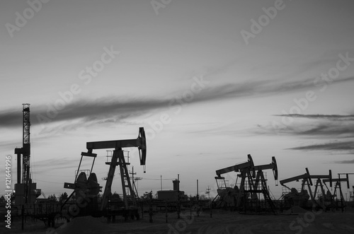 Foto Pump jacks and derrick silhouette during sunset in the oilfield
