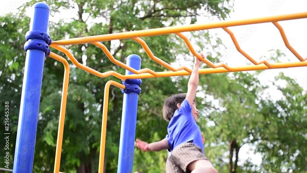 Slow motion, Young asian boy hang the yellow bar by his hand to exercise at out door playground under the big tree