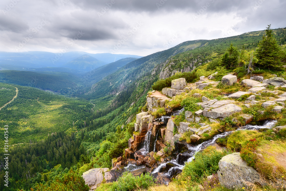 Fototapeta premium Piękny wodospad nad głęboką zieloną doliną z górami