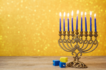 Jewish holiday Hanukkah background with vintage menorah and spinning top dreidel over lights bokeh.